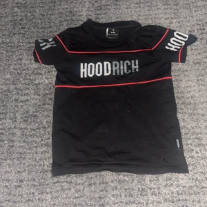 Svart t-shirt från Hoodrich - Snygg svart t-shirt från Hoodrich med vita bokstäver och röda detaljer. Perfekt för en casual look. Kortärmad och tillverkad i ett bekvämt material.