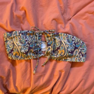 Mönstrad bikiniöverdel - Snygg bikiniöverdel med färgglatt paisleymönster i grönt, blått och orange. Den har knytband för justerbar passform och en stilren design utan axelband. Perfekt för en dag på stranden eller vid poolen! Använd en gång! 