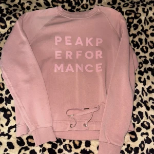 Peak Performance - Säljer en rosa tröja från Peak Performance med tryck framtill. Tröjan har långa ärmar och snörning nertill.