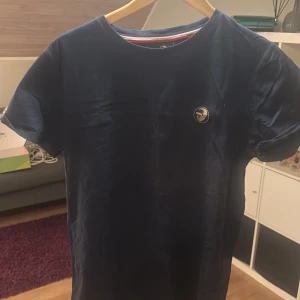 Mörkblå t-shirt från WHO's A.C.E - Säljer en stilren mörkblå t-shirt från WHO's A.C.E med en liten logga på bröstet. T-shirten är kortärmad och har en klassisk rund halsringning. Perfekt för en avslappnad look.