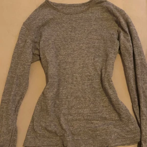 Grå ribbad långärmad tröja - Säljer en stilren grå ribbad tröja med långa ärmar. Perfekt för en avslappnad look. Tröjan har en enkel design som gör den lätt att matcha med olika outfits.