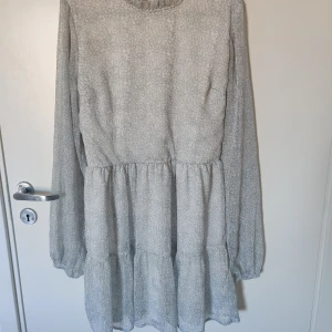 Ljusblå mönstrad klänning - Säljer en söt ljusblå klänning med ett diskret blommönster. Klänningen har långa ärmar och en luftig passform med volanger i kjolen.