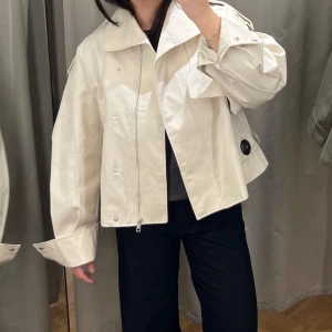 Kort beige trenchcoat från &OtherStories - Ljusbeige trenchcoat med dragkedja från &OtherStories. 🌸Jackan har en lös passform och långa ärmar. 👚 Perfekt för vår och höst. 🌷Finns ett tillhörande skärp. Använd, men i mycket bra skick! Nypris runt 1300kr.