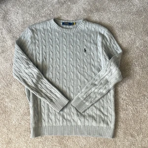 Grå stickad tröja från Polo Ralph Lauren - Säljer en stilren grå stickad tröja från Polo Ralph Lauren med kabelstickat mönster. Självklart äkta. 