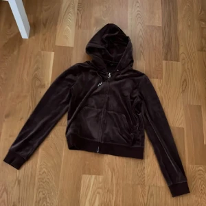 Brun hoodie från Juicy Couture str M men passar S - Säljer en snygg brun hoodie från Juicy Couture str M men passar S Mjukt material. Den har en dragkedja framtill och en broderad logga på bröstet. Perfekt för en avslappnad stil.