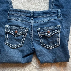 Blå jeans från Gina Tricot - Snygga blå jeans från Gina Tricot med bootcut-stil. De har dekorativa bakfickor med knappar och kontrastsömmar. Perfekta för en avslappnad look. Kan fixa bättre bild