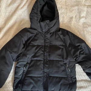 Svart pufferjacka från Pull&Bear - Säljer en svart pufferjacka från Pull&Bear. Jackan har en huva och stängs med både dragkedja och knappar. Perfekt för kalla dagar då den håller värmen jättebra. Använd men i fint skick🤍