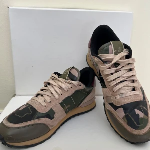 Valentino Garavani Rockrunners sneakers i camouflage - Snygga Valentino Garavani Rockrunners sneakers med ett coolt camouflage-mönster i grönt och beige. Skorna har snörning och en bekväm sula med bra grepp. Perfekta för en trendig look.