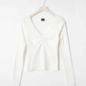 Vit långärmad topp från Gina Tricot - Säljer en stilren vit långärmad topp från Gina Tricot med v-ringning och en snygg rynkdetalj framtill. Perfekt för en enkel och elegant look. Passar bra till både jeans och kjol.