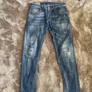 Dondup jeans - Säljer ett par blå jeans från Dondup med slitna detaljer och en klassisk femficksdesign. Jeansen har en knappgylf och är i en straight passform. Perfekta för en avslappnad stil.