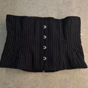 Svart randig korsett/Black striped corset, underbust  - Snygg svart korsett med smala vita ränder och knäppning framtill. Snörning på baksidan för att justera passform/göra den tightare. Endast använd ett fåtal gånger. Köpt på Chamber of Love. Nypris ca 850kr.