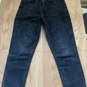 Svarta jeans från Gina tricot - Snygga svarta jeans från Gina tricot med knappgylf och klassisk femficksdesign. Perfekta för en stilren look. Passar till många olika outfits och tillfällen.