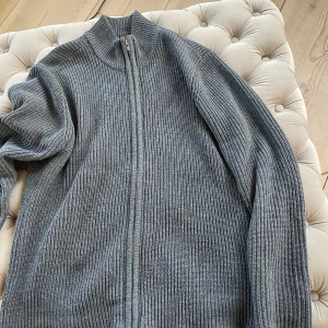 Grå ribbad kofta med dragkedja - Säljer en stilren grå ribbad kofta med dragkedja. Perfekt för kyliga dagar och enkel att matcha med olika outfits. Koftan har långa ärmar och en hög krage för extra värme.