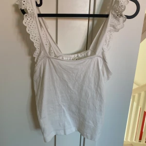Vit linnetopp med spetsdetaljer - Säljer en söt vit linnetopp med spetsdetaljer på axelbanden. Perfekt för varma sommardagar. Toppen har en enkel och stilren design som passar till många olika outfits.