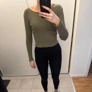 Olivgrön ribbad tröja från Gina Tricot - Säljer en superfin olivgrön ribbad tröja från Gina Tricot. Den har en croppad stil och långa ärmar, perfekt för både höst och vår. Tröjan är i bra skick och passar perfekt till ett par jeans eller kjol. Skön och stilren design som funkar till det mesta!