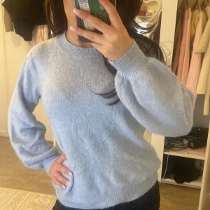 Ljusblå stickad tröja - Säljer en mysig ljusblå stickad tröja med rund hals och långa ärmar. Perfekt för kyliga dagar och enkel att matcha med olika outfits. Tröjan har ribbade muddar vid ärmslut och nederkant.