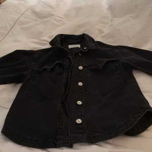 Svart jeansjacka med nitar - Snygg svart jeansjacka med silverfärgade knappar och coola nitar på baksidan och ärmarna. Jackan har en klassisk krage och två bröstfickor. Dock skulle jag säga att den är större i stoleken