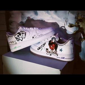 Unika handmålade sneakers - Snygga vita Nike sneakers med unika handmålade motiv. Skorna har coola illustrationer i svart, rött och blått, inklusive stjärnor och text. Perfekta för dig som vill sticka ut med en personlig stil.