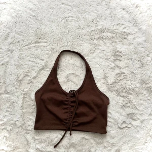 Brun ribbad halterneck topp - Säljer en snygg brun ribbad halterneck topp med knytning framtill. Perfekt för en trendig look. Passar bra till både jeans och kjol.