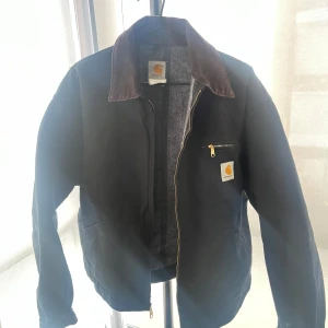 Svart jacka från Carhartt - Säljer nu en svart jacka från Carhartt, Nu när våren har börjat inta sakta men säkert. Jackan har en brun krage och dragkedja framtill. En bröstficka med dragkedja och Carhartt-logga. Lite mer vintage vibe till den, Passar folk med L och M i storlek beroende på hur man vill att den sitter. M för lite mer Baggy. Den har en boxig struktur då den är lite längre i bredden. Kontakta vid frågor eller fler bilder! :)