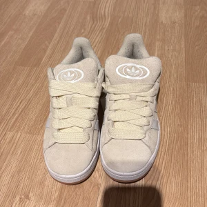 Beige sneakers från Adidas - Snygga beige sneakers från Adidas med klassiska tre ränder i vitt på sidan. Skorna har en rund tå och breda snören för en cool look. Perfekta för en avslappnad stil.