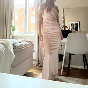 Balklänning Champagnefärgad axelbandslös långklänning - Elegant champagnefärgad långklänning med en one-shoulder design. Klänningen har en slät och glansig yta som ger en lyxig känsla. Perfekt för balen. Nu den inte kommer till användning för mig längre💗original priset är 3800kr men säljer för 1500kr