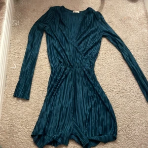 Mörkgrön omlottklänning från NLY Trend - Snygg mörkgrön omlottklänning från NLY Trend i ett plisserat material. Klänningen har långa ärmar och en elegant omlottdesign som ger en smickrande passform. Perfekt för en stilfull look!