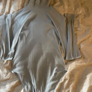 Ljusblå ribbad polobody - Säljer en stilren ljusblå polobody med ribbad struktur. Tröjan har långa ärmar och en hög krage, perfekt för kyligare dagar. Den är både bekväm och snygg, och passar bra till jeans eller kjol. 