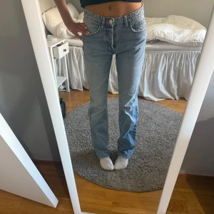 Ljusblå raka jeans - Säljer ett par klassiska ljusblå jeans med hög midja och rak passform. De har en traditionell femficksdesign och stängs med dragkedja och knapp. Perfekta för en avslappnad stil.