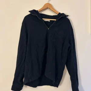 Svart långärmad tröja med dragkedja - Säljer en svart långärmad tröja med dragkedja och bröstficka. Perfekt för en avslappnad stil. Tröjan har en krage som kan bäras uppvikt eller nedvikt.