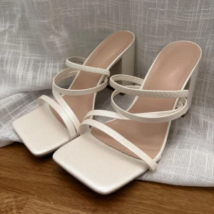 Vita sandaler med klack - Eleganta vita sandaler med fyrkantig tå och blockklack. De har tunna remmar som korsar över foten för en stilren look.