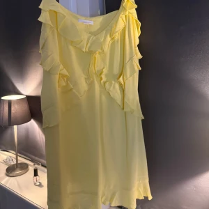 Gul klänning med volanger - Säljer en söt gul klänning med volanger. Klänningen har en lösare passform och kort längd, vilket gör den luftig och bekväm. Perfekt nu inför sommaren till midsommar och andra firanden. Klänningen är bara använd en gång