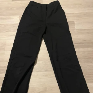 Svarta kostymbyxor - Snygga svarta kostymbyxor med en klassisk design. De har en rak passform och är perfekta för en stilren look. Byxorna har hällor för bälte och en diskret dragkedja framtill! 