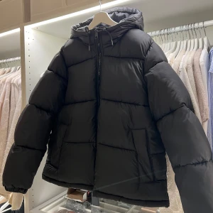 Svart pufferjacka från H&M  - Säljer en svart pufferjacka med huva och dragkedja. Jackan har långa ärmar och en bekväm passform, perfekt för kyliga dagar. Den är stilren och enkel att matcha med olika outfits.