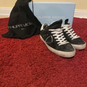 Svarta sneakers från Philippe Model - Snygga svarta sneakers från Philippe Model med vita snören och en vit sula. Skorna har en stilren design med diskreta detaljer och är perfekta för en avslappnad look.