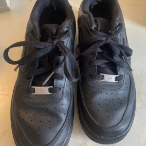 Svarta Nike Air Force 1 - Säljer ett par klassiska svarta Nike Air Force 1 med snörning. Skorna har en stilren design med perforerade detaljer på tån och en robust sula. Perfekta för en casual look. Beställde dom på Vinted för 700kr, men kom inte till användning då hon som sålde lurade mig. Hon sa att dom var stl 40 men är egentligen stl 38. Dom är i mycket bra skick!