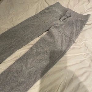 Grå mjukisbyxor från Juicy Couture - Säljer ett par grå mjukisbyxor från Juicy Couture i storlek XS. Byxorna har en bekväm passform med snörning i midjan och praktiska fickor både fram och bak. Perfekta för en avslappnad stil.