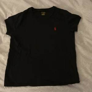 Svart t-shirt från Ralph Lauren - Säljer en klassisk svart t-shirt från Ralph Lauren med det ikoniska röda broderade logotypen på bröstet. Inga defekter använd 1 gång. Skriv om några funderingar.