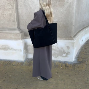 Stor svart axelväska i mocka-look - Säljer en stor svart axelväska med enkel och stilren design. Väskan har långa axelband och rymmer enkelt en laptop. Perfekt för dig som vill ha plats med mycket i vardagen. Materialet ser ut som mocka och väskan är helsvart. Paketet är inte uppburtit, alltså helt ny. Säljer då det var svårt att göra en retur: nypris 530, mitt pris 400