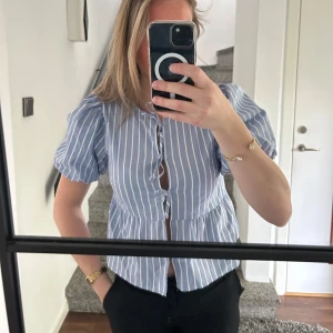 Blåvit randig blus med puffärm - Säljer en blå och vit randig blus med korta puffärmar och knappar framtill. Fin till sommaren. Aldrig använd, då den är i väldigt bra skick