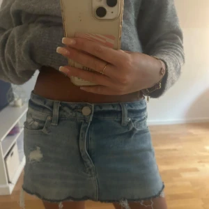 Ljusblå jeanskjol med rå kant - Säljer en ljusblå jeanskjol med rå, fransig nederkant och slitningar framtill. Kjolen har klassiska fem fickor och bälteshällor. Perfekt för en avslappnad och trendig look.