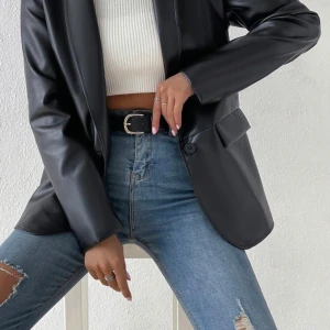 Svart skinnkavaj - Snygg svart kavaj i skinnimitation med klassisk krage och långa ärmar. Kavajen har en oversized passform och stängs med en knapp framtill. Perfekt att styla till jeans eller kjol för en trendig look.