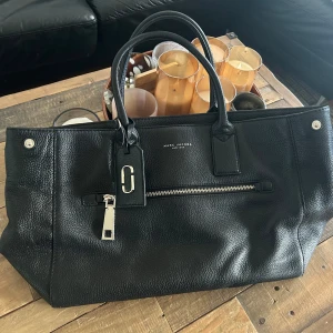  Marc Jacobs Gotham tote  - Säljer en svart handväska från Marc Jacobs i skinn med silverfärgade detaljer och dragkedja framtill. Väskan har dubbla handtag och en klassisk, stilren design. Perfekt för dig som vill ha en rymlig och snygg accessoar till vardagen. Köparen står för frakten . Betalning sker i förskott via Swish 🤩