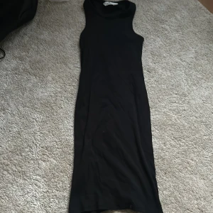 Svart långklänning från H&M - Säljer en svart långklänning från H&M med ärmlös design och hög hals. Klänningen har en tight passform och är tillverkad i ett mjukt, stretchigt material som sitter snyggt på kroppen. Perfekt för dig som gillar stilrena och enkla plagg.
