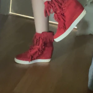 Röda sneakers med fransar - Säljer ett par röda sneakers med kilklack och vita sulor. Skorna har dekorativa fransar längs sidorna och framtill, vilket ger dem en unik och trendig look. Passar perfekt med Stockholm stilen ❤️