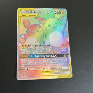 Raichu & Alolan Raichu GX TAG TEAM Pokémonkort - Säljer ett holografiskt Pokémonkort: Raichu & Alolan Raichu GX TAG TEAM med 260 HP. Kortet har färgglad design med guld- och regnbågseffekt, samt attacker som Tandem Shock och Lightning Ride GX. Perfekt för samlare eller Pokémon TCG-spelare.