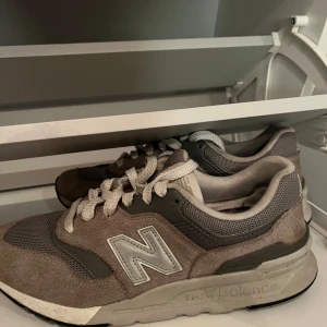 Gråa sneakers från New Balance - Säljer ett par gråa New Balance sneakers med vit sula och vita snören. Skorna har meshdetaljer och mockapartier samt den klassiska N-loggan på sidan. Perfekta för en avslappnad och sportig stil. Pris kan diskuteras.