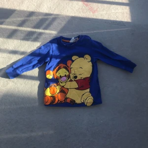 Blå långärmad tröja med Nalle Puh och Tiger - Säljer en blå långärmad tröja med stort tryck av Nalle Puh och Tiger på framsidan. Perfekt för dig som gillar klassiska Disney-karaktärer och vill ha en färgglad och lekfull stil.