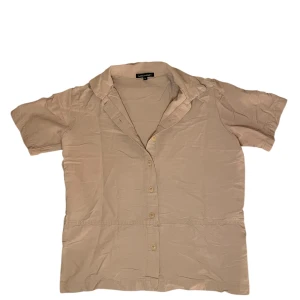 Machine skjorta - Säljer en stilren beige/cremevit skjorta från Machine. Skjortan har korta ärmar, klassisk krage och knäppning framtill med matchande knappar. Perfekt för en avslappnad och snygg look. Skjortan har Storlek M men den passar mer som storlek S.