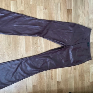 Vinröda skinnbyxor från Gina Tricot - Snygga vinröda skinnbyxor från Gina Tricot i flare/bootcut passform och medel/låg midja. Byxorna har dragkedja och hyska fram samt fickdetaljer med en mjuk insida. Perfekta för att lyfta din outfit med en trendig touch.